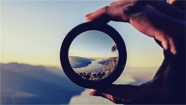 A hand holding a lens in front of a lake